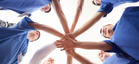Medizinisches Personal legt die Hände übereinander, um ihren Teamgedanken zu bekräftigen