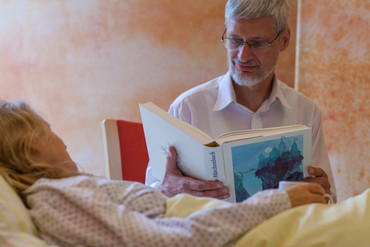 Ehrenamtlicher liest eienr schwerkranken Patientin auf der Palliativstation vor